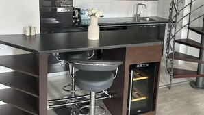 Een moderne keuken met een centraal eiland, barkrukken en een stalen trap.