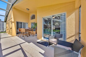 A covered patio with outdoor furniture, a sliding glass door leading to a backyard, and a small awning over the door.