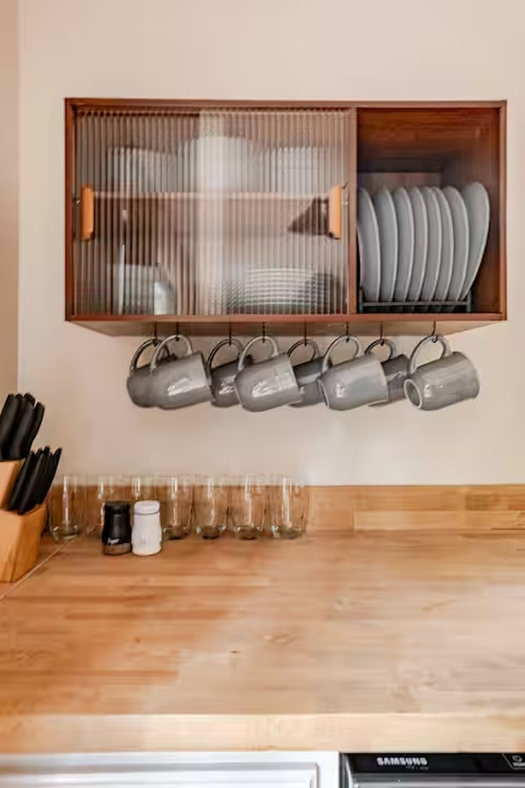 A kitchen with a wooden cabinet shelf holding plates and a row of mugs.