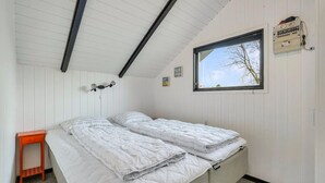Quarto com duas camas, uma janela, luminária fixada na parede e uma pequena mesa laranja.