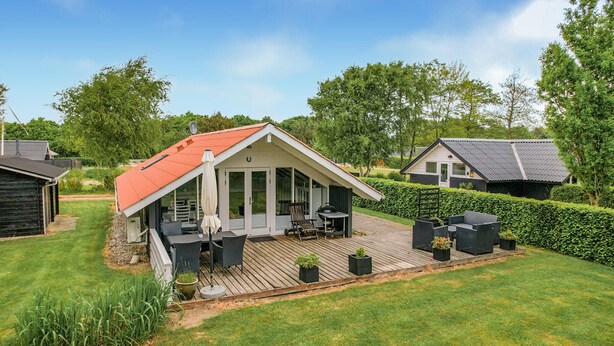 Uma casa com telhado inclinado, um deck com mobiliário de exterior e um gramado bem cuidado.