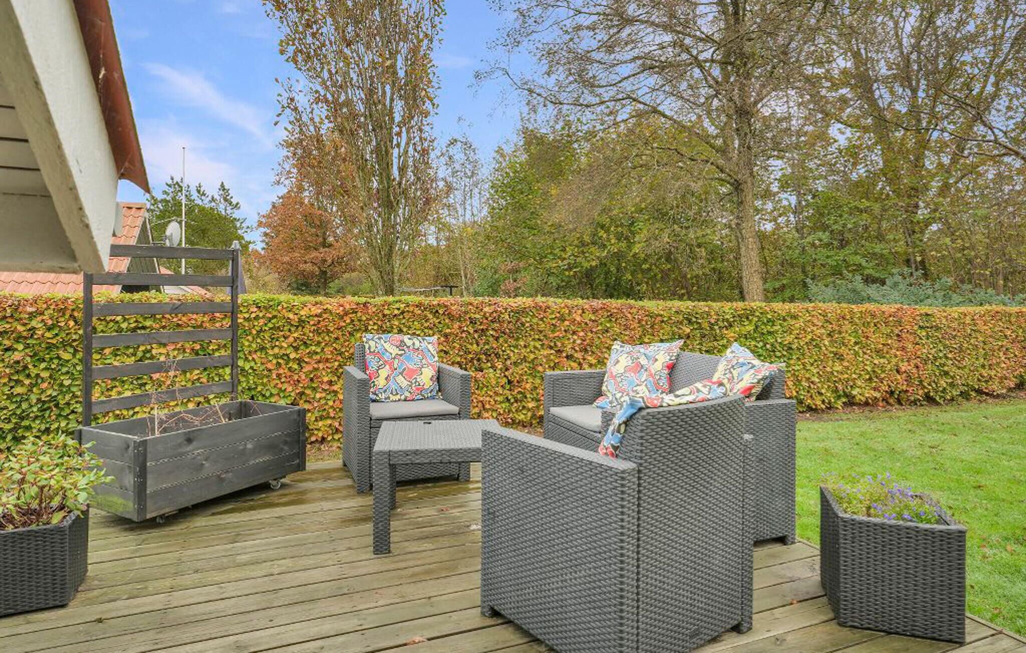 An outdoor patio with wicker furniture, a wooden deck, and a hedge in the background.