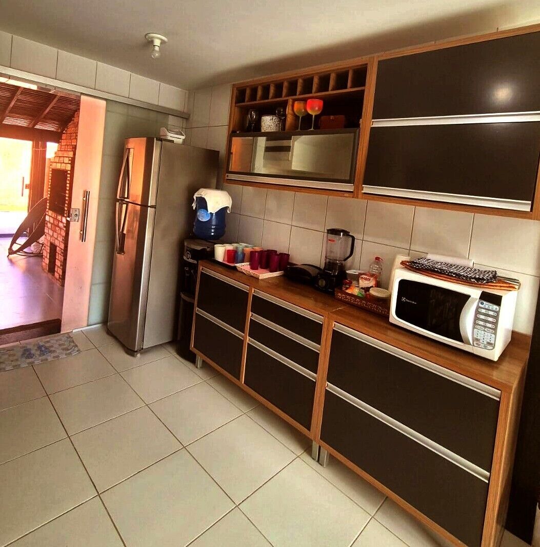 A kitchen with a refrigerator, microwave, and a shelf with various items.