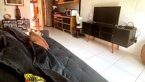 A living room with a sofa, a television, and a kitchen area in the background. - Casa Magister Atalaia (Salinópolis)