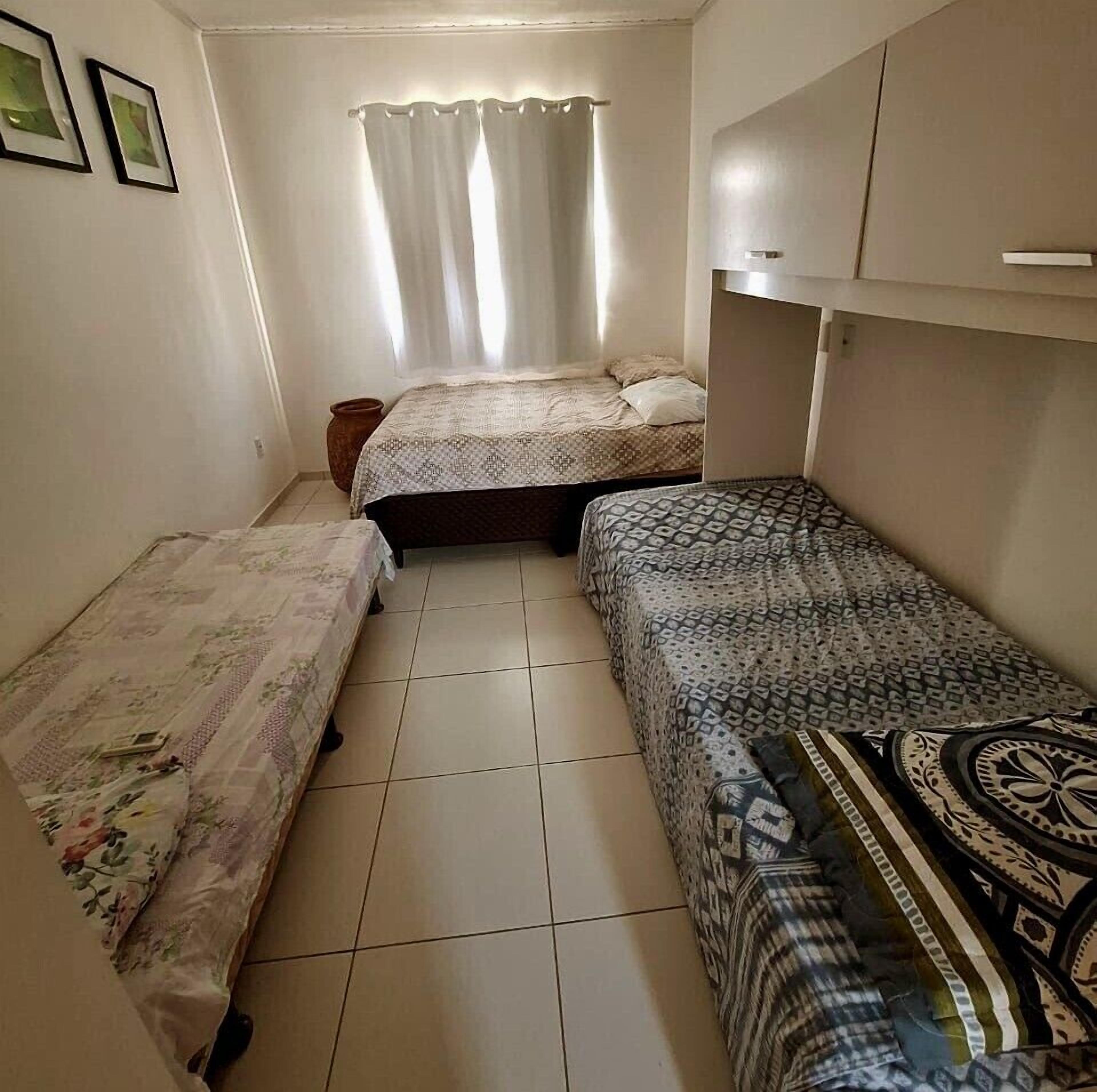 Una habitación pequeña y funcional con dos camas individuales, una ventana con cortinas y piso de baldosas.