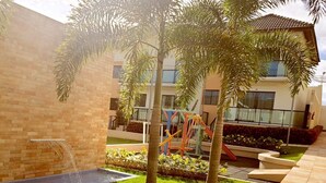 A courtyard with a water feature, palm trees, and a playground. - Casa Magister Atalaia (Salinópolis)