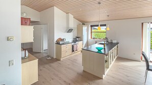Une cuisine moderne avec un plancher en bois, un îlot central et une fenêtre donnant sur un espace verdoyant.