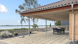 Un patio couvert avec vue sur un lac, doté d’un sol en briques, d’une clôture en bois et de mobilier d’extérieur.