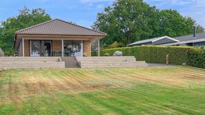 Une maison dotée d’un patio couvert, d’un escalier en briques et d’une pelouse bien entretenue.