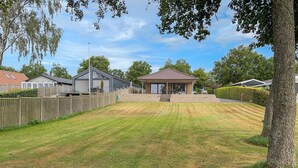 Un jardin à l’arrière d’une maison, comprenant une terrasse couverte, un espace clôturé et une pelouse.