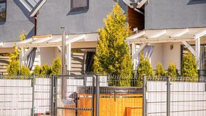 Ein Wohngebäude mit überdachter Terrasse, einem Holzzaun und einem großen Nadelbaum.