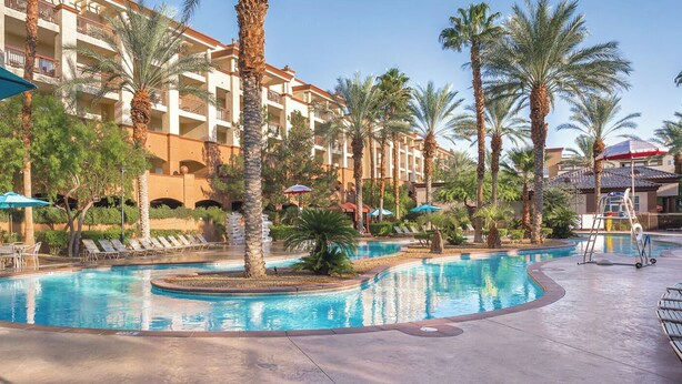 Ein Poolbereich eines Resorts mit Palmen, Liegestühlen und Sonnenschirmen.
