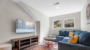 A modern living room with a large flat-screen TV, a blue sofa, a wooden entertainment unit, and a colorful rug. - Perfect Location! Near SDC, Branson Strip & Lake (Branson)