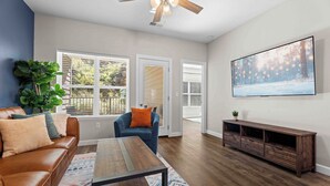 A living room with a brown leather sofa, a blue armchair, a wooden coffee table, and a large flat-screen TV on the wall. - Perfect Location! Near SDC, Branson Strip & Lake (Branson)