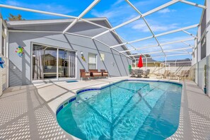 A swimming pool area with a covered patio, lounge chairs, and a red umbrella. - 4 Bedroom Private Pool Home with Themed Rooms (Davenport)