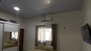 A bedroom with a bed, a wardrobe, an air conditioning unit, and a window with curtains.
