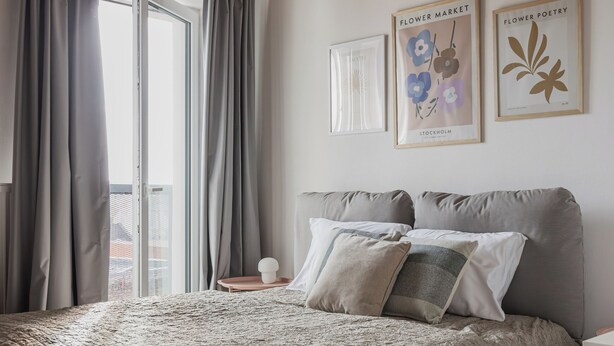 Een slaapkamer met een groot bed, houten balken in het plafond, een raam met gordijnen en twee ingelijste foto's aan de muur.