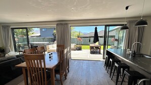 Ein geräumiger Wohnbereich mit einem Holzessttisch und Stühlen, einer Küche mit dunkler Arbeitsplatte und einer Glastür, die auf eine Terrasse mit Gartenmöbeln führt.