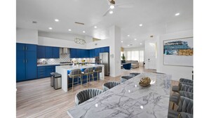 Een moderne keuken met blauwe kastjes, een centraal eiland met barkrukken en een marmeren aanrecht.
