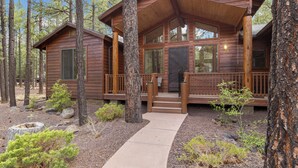 Un chalet rustique avec une façade en bois, une véranda et un chemin en béton menant à l’entrée.