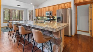 Une cuisine dotée d’un îlot en granit, de meubles en bois, d’appareils électroménagers en acier inoxydable et d’un mur d’accent en pierre.