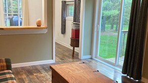 A living room with a plaid sofa, a wooden coffee table, a laundry room sign, and a view of a grassy yard through large windows. - Newly renovated 3-bedroom 2 bath pet friendly unit on Barclay Mountain. (Monroe)