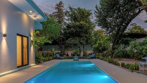 Ein moderner Poolbereich im Freien mit einem klaren blauen Pool, umgeben von üppiger Vegetation und einem gepflegten Garten.