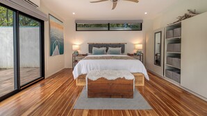 Ein modernes Schlafzimmer mit einem großen Bett, Holzboden, Deckenventilator und Blick durch eine Schiebetür.