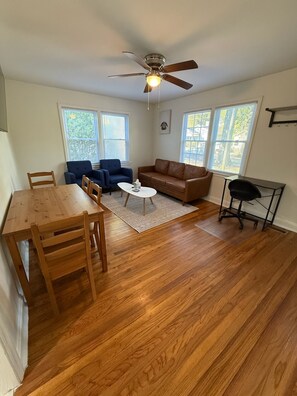 A spacious living room with a wooden dining table, blue armchairs, a brown leather sofa, and a ceiling fan.