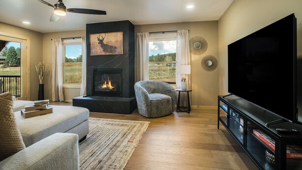 A modern living room with a fireplace, comfortable seating, a flat-screen TV, and a view of the outdoors. - Alpenglow Aura in Angel Fire (Angel Fire)