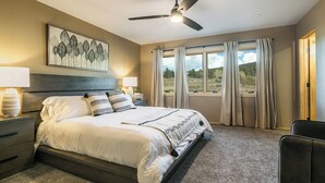 A bedroom with a bed, nightstands, a ceiling fan, a window with curtains, and a view of the outdoors. - Alpenglow Aura in Angel Fire (Angel Fire)