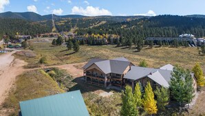 A large lodge with multiple floors and a prominent roof, surrounded by a forested area and mountains in the background. - Alpenglow Aura in Angel Fire (Angel Fire)