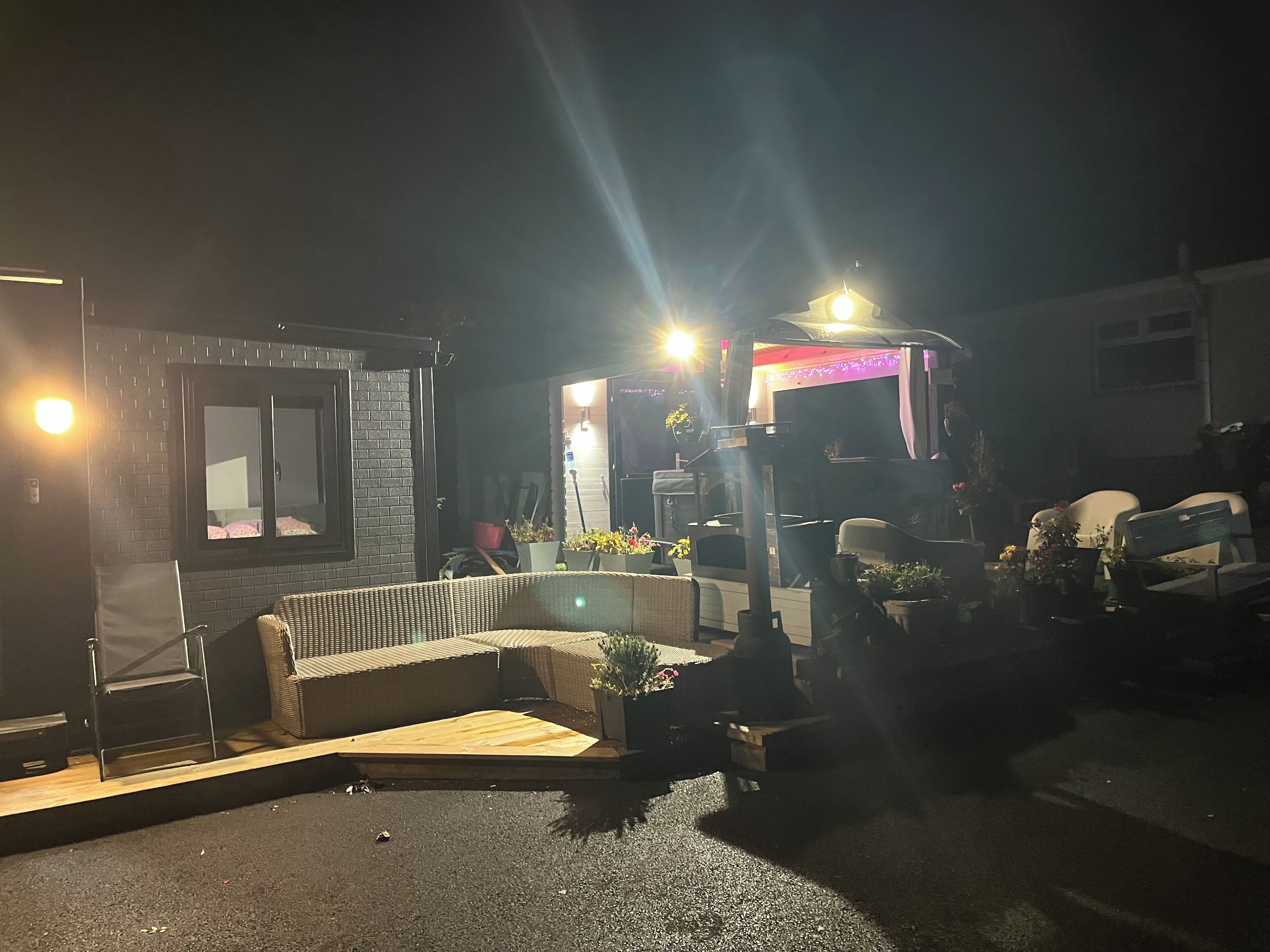 Ein Außenbereich mit Sitzgelegenheiten bei Nacht, mit einer Couch, Sesseln, einem kleinen Tisch und Topfpflanzen.
