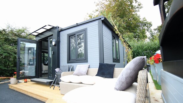 Een modern, compact huis met een patio, voorzien van rieten meubilair en een auto in de buurt.