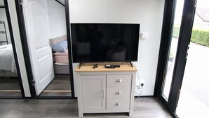 Een kamer met een televisie op een houten kast, een bed met kussens, en een deur die naar buiten leidt.
