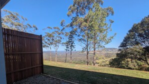 A backyard with a wooden fence, a grassy lawn, and a view of trees and hills. - Maleny-Montville Cottages #4 - 2 bed with ocean views (Balmoral Ridge)