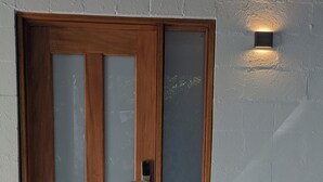 A wooden door with a frosted glass panel and a keyhole, set against a textured wall with a small wall-mounted light fixture. - Maleny-Montville Cottages #4 - 2 bed with ocean views (Balmoral Ridge)