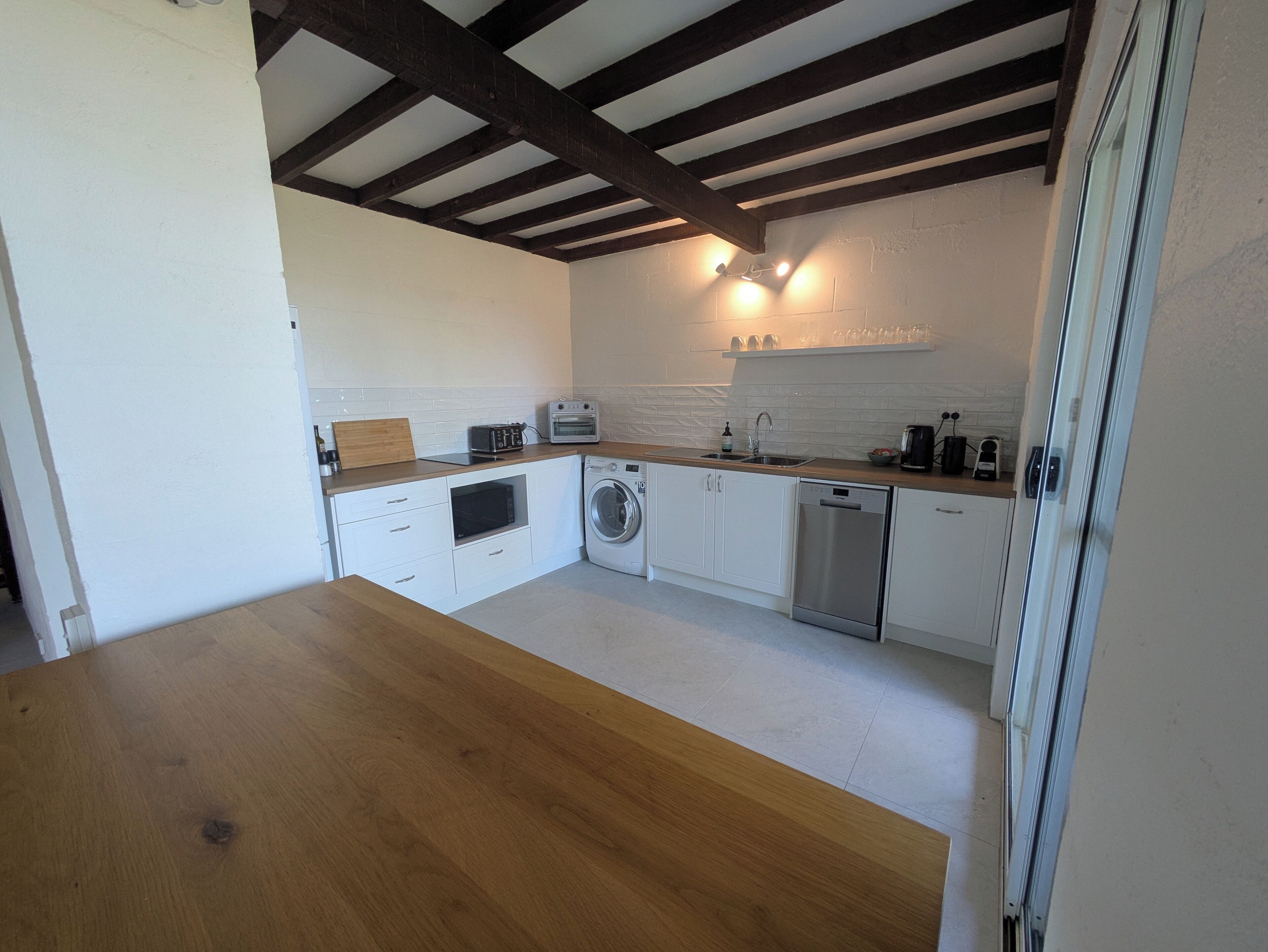 A modern kitchen with white cabinets, a wooden countertop, a washing machine, a dishwasher, and a built-in oven.