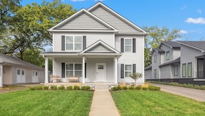 A two-story house with a front porch, a small front yard, and a driveway leading to the entrance. - The Stadium Getaway (Lexington)