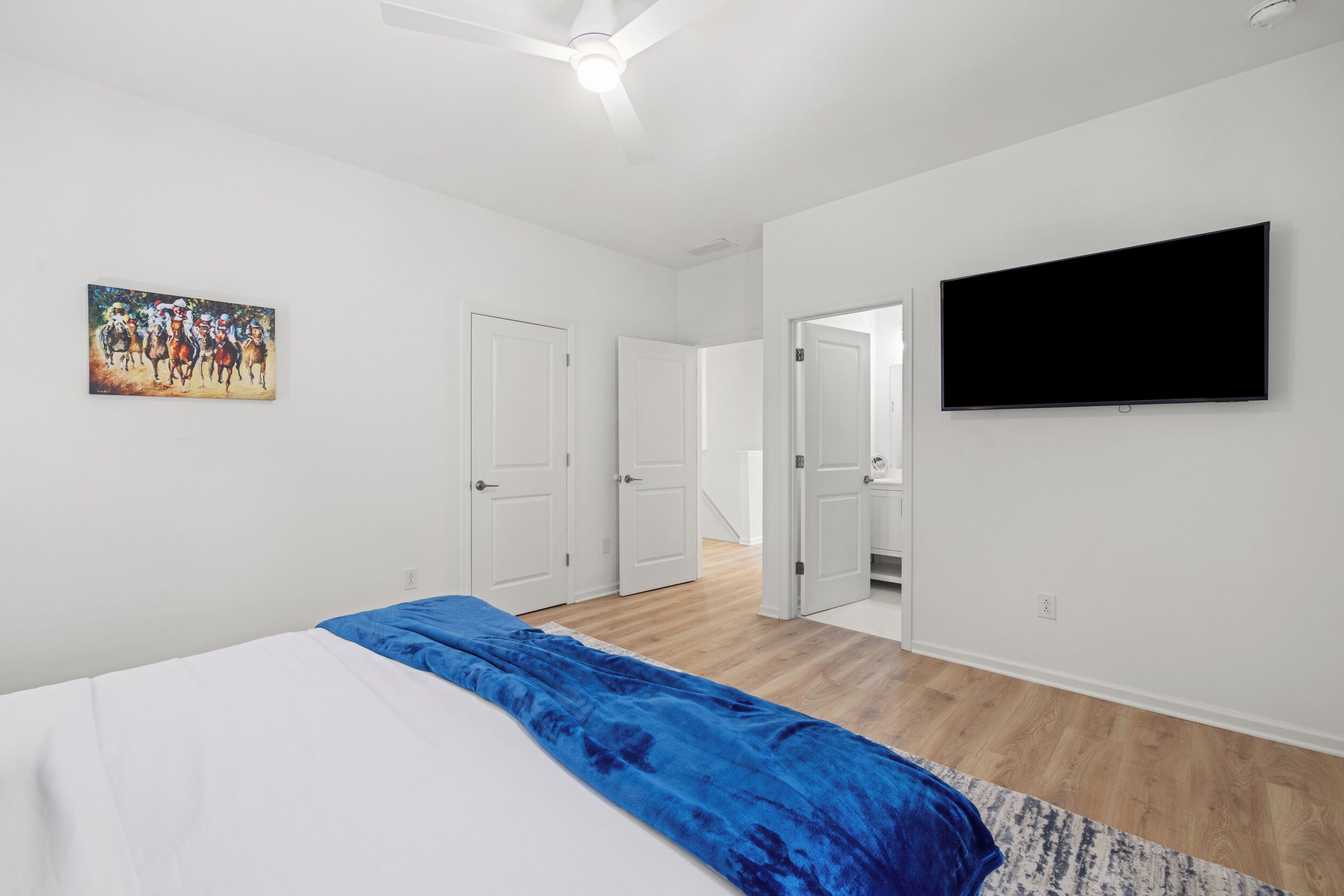 A bedroom with a bed, a flat-screen TV, and a painting on the wall.