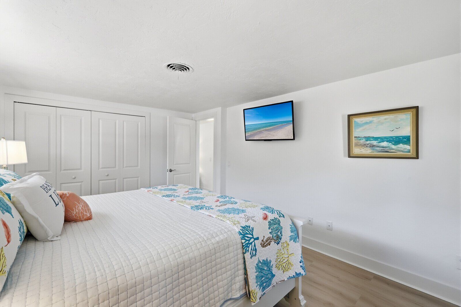 A bedroom with a bed, a nightstand, a wall-mounted TV, and two framed pictures.
