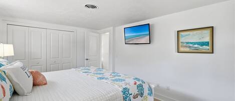 A bedroom with a bed, a nightstand, a wall-mounted TV, and two framed pictures.