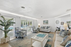 Amplio salón con un ventanal grande, un conjunto de sofás, una mesa de centro y vistas a una piscina exterior.
