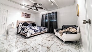 Een slaapkamer met een bed, een bank, een plafondventilator, een nachtkastje en een deur.
