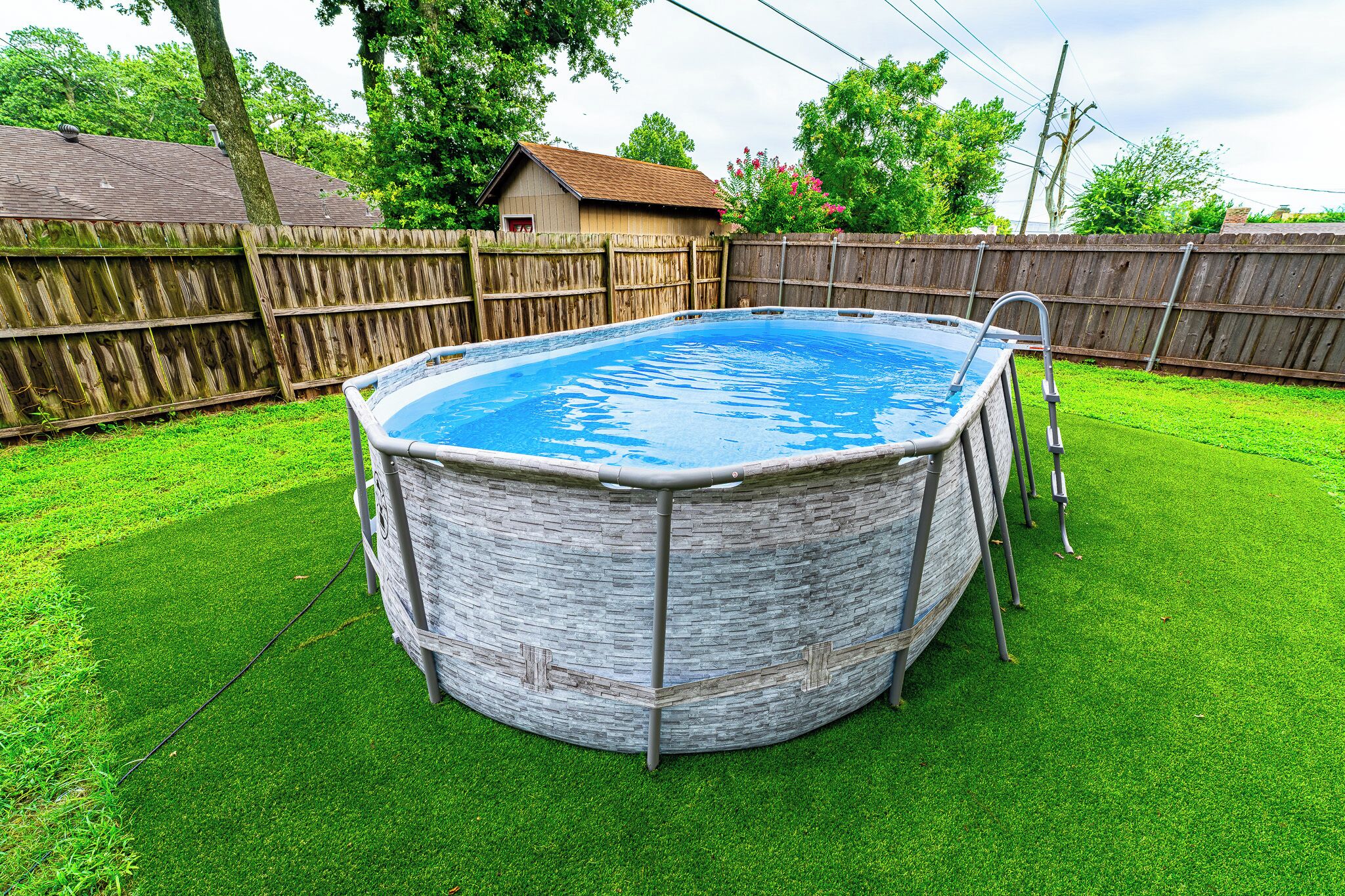 An above-ground swimming pool with a ladder, surrounded by a wooden fence and a grassy yard.