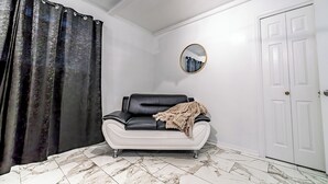 Een kamer met een zwarte leren bank, een witte deur en een spiegel aan de muur.