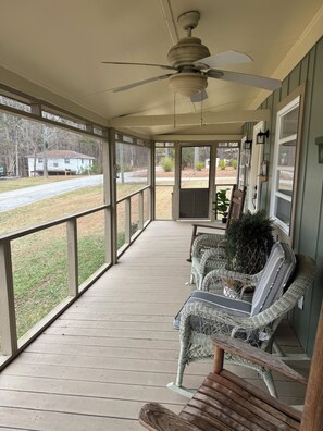A covered porch with wicker furniture, a ceiling fan, and a view of a road and house.