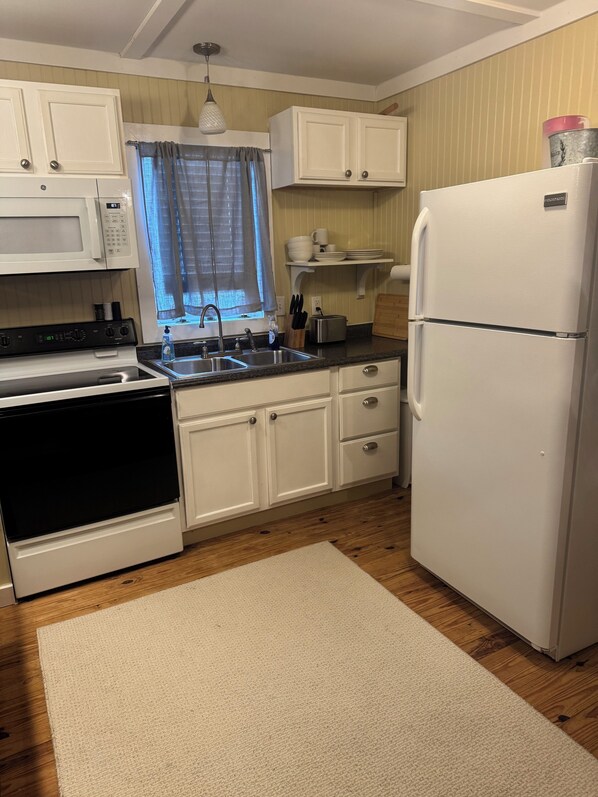 A compact kitchen with white cabinets, a white refrigerator, a stove, and a sink.