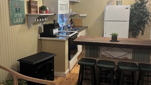 Una cocina compacta con una isla central, horno integrado, refrigerador y pileta. Hay taburetes de bar y una mesita.
