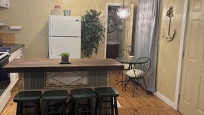 Una cocina compacta con una isla central, taburetes de bar, un refrigerador y un comedor con una silla y una mesa.